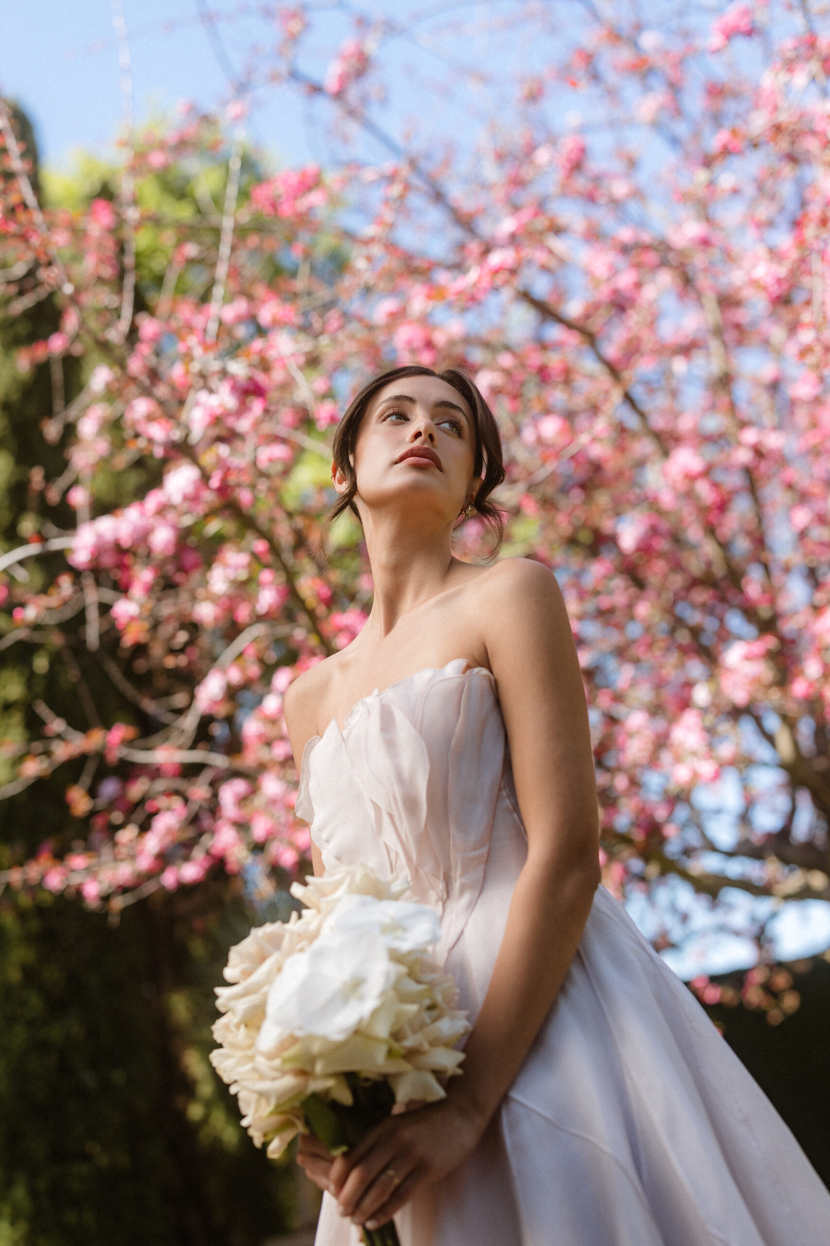 GRACE standing under a pink blossom tree at Mandalay House and Garden wearing Paolo Sebastian